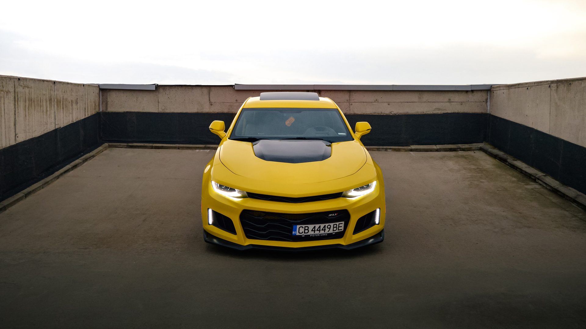Жълт Chevrolet Camaro 2SS отпред, фарове светят, бетонен покрив